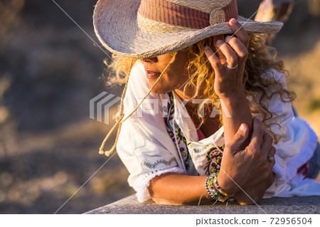 Portait of beautiful young trendy woman with cowboy hat and accessories like bracelets lay down on a wall bench enjoying the sunset light - people in outdoor leisure activity and vacation time Portait of beautiful young trendy woman with cowboy hat and accessories like bracelets lay down on a wall bench enjoying the sunset light - people in outdoor leisure activity and vacation time 72956504