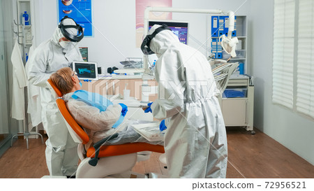 Dentist in protective equipment reviewing x-ray using tablet Dentist in protective equipment reviewing x-ray using tablet 72956521