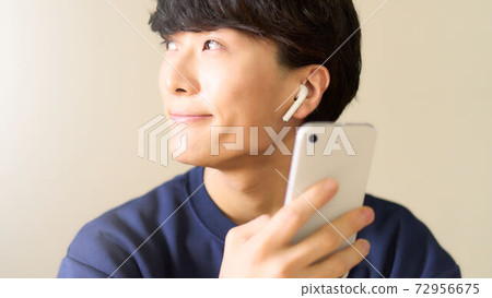 A young man with a smartphone wearing wireless earphones 72956675