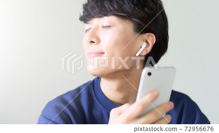 A young man with a smartphone wearing wireless earphones 72956676