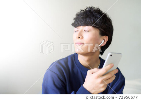 A young man with a smartphone wearing wireless earphones 72956677