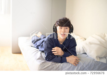 Young man wearing headphones on the bed 72956678