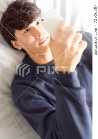 Young man looking at a smartphone on the bed 72956687