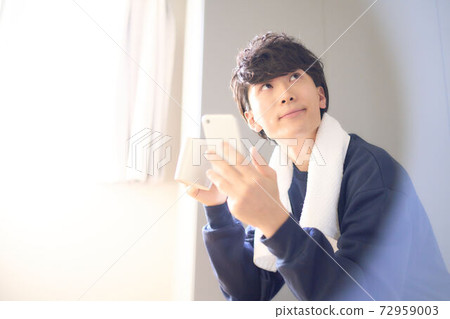 Young man holding a smartphone and a mug 72959003