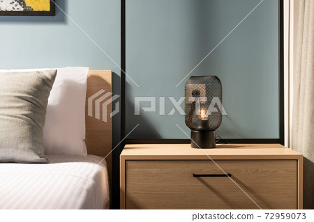 Closeup of modern black metal edison bulb lamp on wooden bedroom night table in contemporary style gray room interior with pine wood bed and white cotton bedlinen Closeup of modern black metal edison bulb lamp on wooden bedroom night table in contemporary style gray room interior with pine wood bed and white cotton bedlinen 72959073