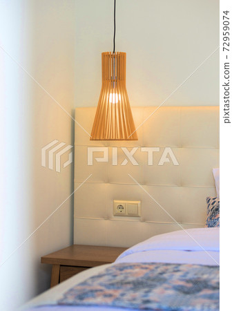 Closeup of beige bedroom night table and wooden hanging lamp, soft leather textile capitone headboard with switch socket Closeup of beige bedroom night table and wooden hanging lamp, soft leather textile capitone headboard with switch socket 72959074