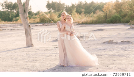Two brides women in white dress with blonde hair hugging each other 72959711