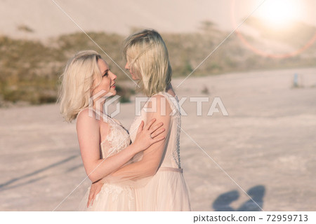 Two brides women in white dress with blonde hair hugging each other 72959713