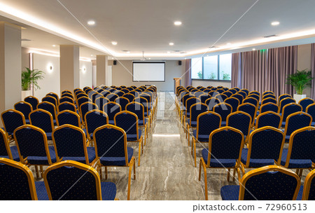 Front view of luxury auditorium interior with empty white screen. Modern conference hall with rows of vintage blue and golden chairs 72960513