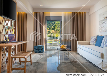 Modern interior of contemporary living room with handmade wicker wood furniture, beige blue soft textile, grey marble tile floor, summer garden view in open French window terrace 72961124