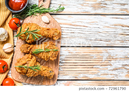 Fried crispy chicken legs, drumstick on a cutting board. White wooden background. Top view. Copy space 72961790