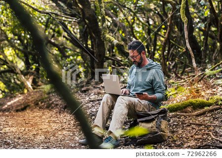 Adult man work with computer laptop and roaming phone connection in the middle of the green wild forest - concept of digital nomad and modern smart working people everywhere internet connected Adult man work with computer laptop and roaming phone connection in the middle of the green wild forest - concept of digital nomad and modern smart working people everywhere internet connected 72962266
