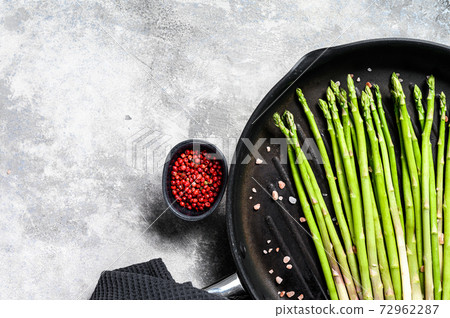 Cooking green asparagus in a frying pan. Black background. Top view. Copy space 72962287