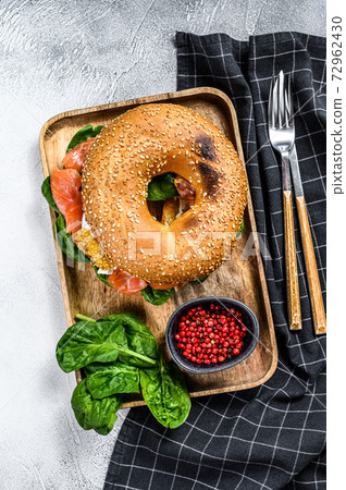 Bagel sandwich with salmon, cream cheese, spinach and egg on a wooden plate. Gray background. Top view 72962430