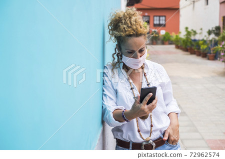 Woman outdoor in the street useing modern phone and wearing protection mask -. coronavirus and covid-19 related new normality lifestyle for people - reading news related outbreak health emergency 72962574