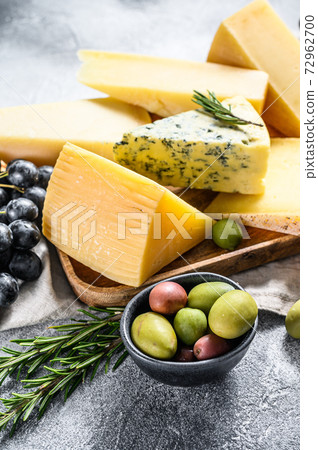 Different pieces of cheese with nuts olives and grapes. Assorted delicious snacks. Gray background. Top view Different pieces of cheese with nuts olives and grapes. Assorted delicious snacks. Gray background. Top view 72962700