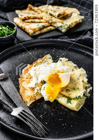 Plate of pancake stuffed with spinach and eggs. Black background. Top view Plate of pancake stuffed with spinach and eggs. Black background. Top view 72963909