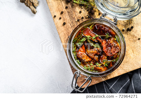 Sun dried tomatoes with herbs and salt in olive oil in a glass. Gray background. Top view. Copy space 72964271