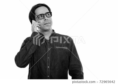 Studio shot of young Persian man talking on mobile phone while thinking 72965642