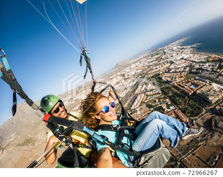 Cheerful happy woman to paraglyde experience with pilot - couple having fun in the air paraglyding over the city with coastline view - tourist and summer holiday vacation active people Cheerful happy woman to paraglyde experience with pilot - couple having fun in the air paraglyding over the city with coastline view - tourist and summer holiday vacation active people 72966267