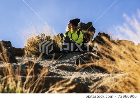 Woman relaxing sit down on the ground after a trekking excursion - concept of travel and outdoor leisure sport hike activity with caucasian people enjoying the nature - blue sky background Woman relaxing sit down on the ground after a trekking excursion - concept of travel and outdoor leisure sport hike activity with caucasian people enjoying the nature - blue sky background 72966906