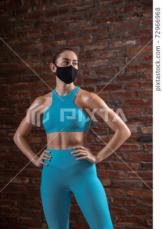 Professional female athlete training on brick wall background wearing face mask. Sport during quarantine Professional female athlete training on brick wall background wearing face mask. Sport during quarantine 72966968