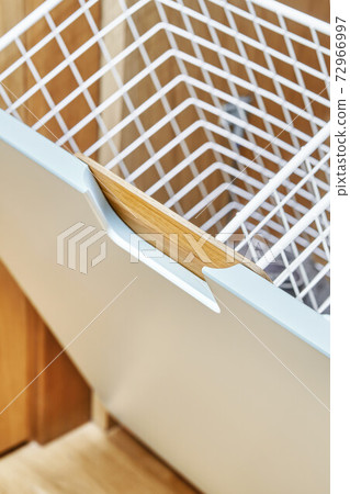 Modern wardrobe with opened metal mesh laundry basket. Wooden wardrobe with light gray cabinet doors. Close-up 72966997