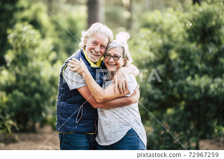 Beautiful elderly lifestyle senior couple hug and stay in love touching during outdoor leisure activity in the wood forest - green nature background and happy old people together 72967259