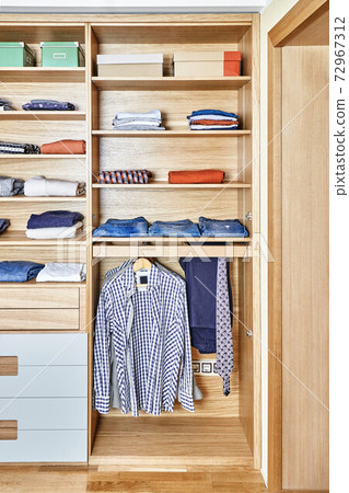 Modern wardrobe with clothes hanging on slide out racks and folded on the shelves. Modern furniture 72967312