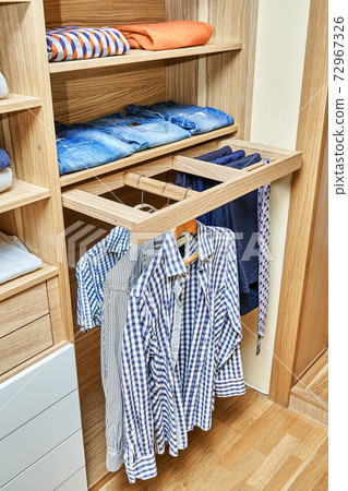 Modern wardrobe with clothes hanging on slide out racks and folded on the shelves. Modern furniture 72967326