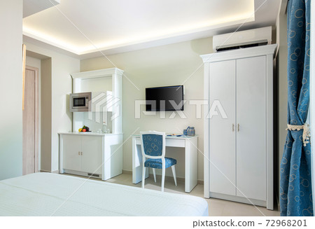 Classic style white and blue interior of hotel room with kitchen module cupboard cabinet, wardrobe and TV table in single space of modern small studio apartment flat 72968201