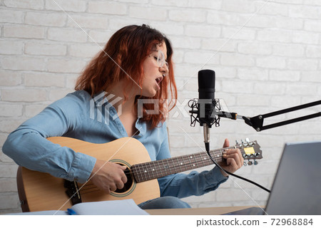 A woman sings into a microphone and plays the guitar live on a laptop. Girl musician recording a video blog A woman sings into a microphone and plays the guitar live on a laptop. Girl musician recording a video blog 72968884