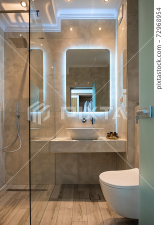 Front view of modern beige marble bathroom with vessel bowl sink, mirror back light, glass shower cabin, wall hung toilet, wooden floor 72968954