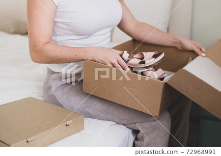 Happy woman unpacks online shopping for shoes. The girl received the package and opens it while sitting in the bedroom Happy woman unpacks online shopping for shoes. The girl received the package and opens it while sitting in the bedroom 72968991