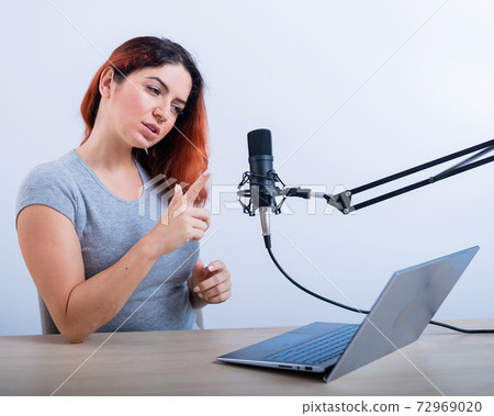 An emotional woman is broadcasting online on a laptop. Female radio presenter at the workplace 72969020