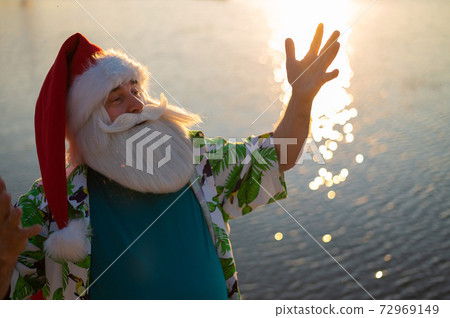 Santa Claus walks along the beach by the sea. Santa is on vacation in a hot country. 72969149