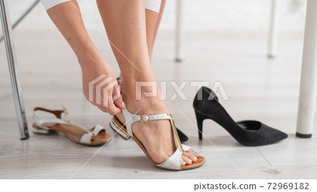 A faceless woman changes her classic shoes into comfortable sandals in the office. A faceless woman changes her classic shoes into comfortable sandals in the office. 72969182
