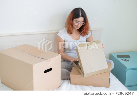 Caucasian woman opens an order while sitting in bed. Online shopping concept with home delivery 72969247
