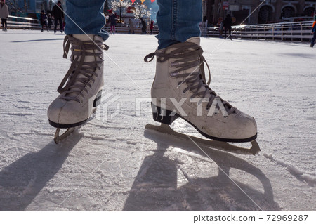 Feet in skates. Public ice-skating rink, pair of skates, scratched ice, sunny day in the winter. Girl skating on ice rink. Close-up photo. Feet in skates. Public ice-skating rink, pair of skates, scratched ice, sunny day in the winter. Girl skating on ice rink. Close-up photo. 72969287