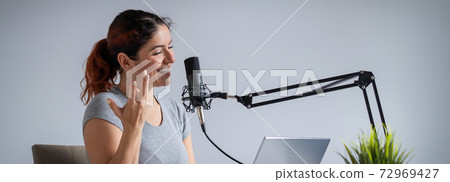 A charming woman radio host is broadcasting live on a laptop. Online radio concept. Wide screen A charming woman radio host is broadcasting live on a laptop. Online radio concept. Wide screen 72969427