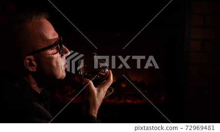 Mature man drinking cognac by the fireplace. Mature man drinking cognac by the fireplace. 72969481