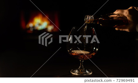 Close-up of a female hand with a glass of brandy on the background of the fireplace 72969491