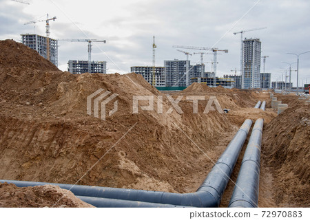 Laying heating pipes in a trench at construction site.  72970883