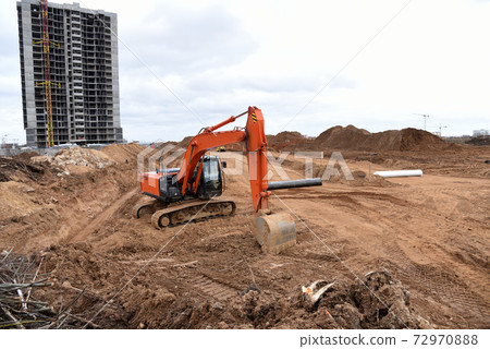 Red excavator during earthmoving at construction site.  72970888