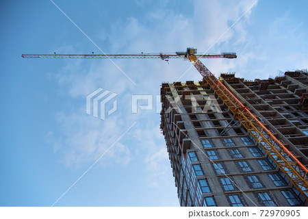 Tower crane working at construction site on blue sky background with white clouds.  Tower crane working at construction site on blue sky background with white clouds.  72970905