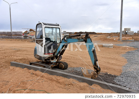 Mini excavator digg trench to lay cables concrete curbs and paving slabs at construction site.  72970935