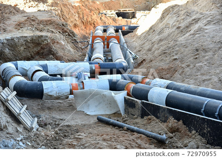 Laying heating pipes in a trench at construction site. 72970955