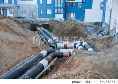 Laying heating pipes in a trench at construction site.  72971271