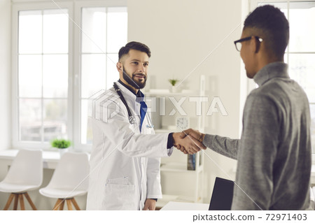 Friendly young doctor welcoming his patient in his office at the clinic or hospital Friendly young doctor welcoming his patient in his office at the clinic or hospital 72971403