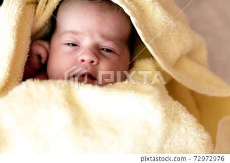 Childhood, care, hygiene, motherhood, innocence concepts - Close up Wet awake Infant newborn after taking shower wrapped in warm yellow towel looking at camera sucks tiny fingers. baby's first bath 72972976